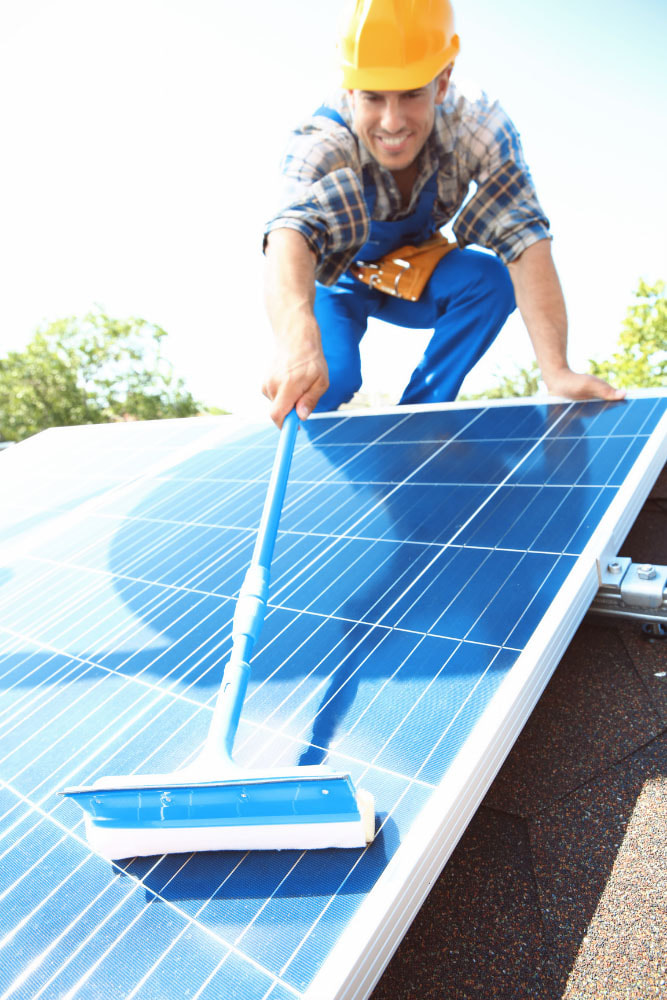 Worker with squeegee washing solar energy system
